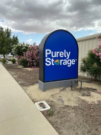 large blue purely storage sign in garden bed among bushes with pink flowers