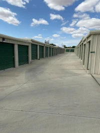 concrete driveway between two tan buildings with many green storage unit doors