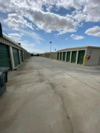 multiple rows of metal self storage buildings containing many green doors and yellow bollards