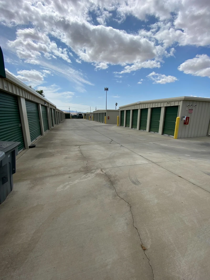 multiple rows of metal self storage buildings containing many green doors and yellow bollards
