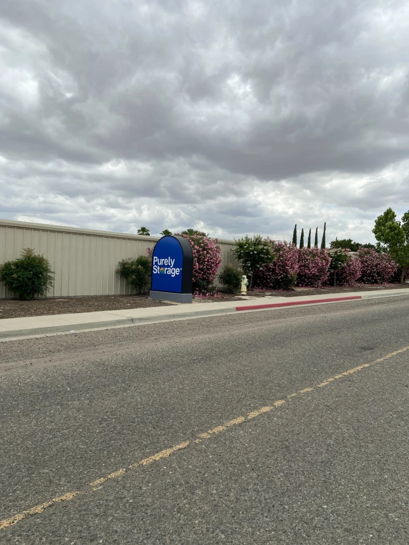 across street view of blue purely storage sign and green bushes with pink flowers