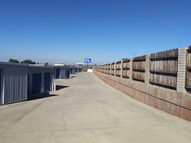 concrete driveway inside storage facility with grey and blue storage units and cinder block outer wall
